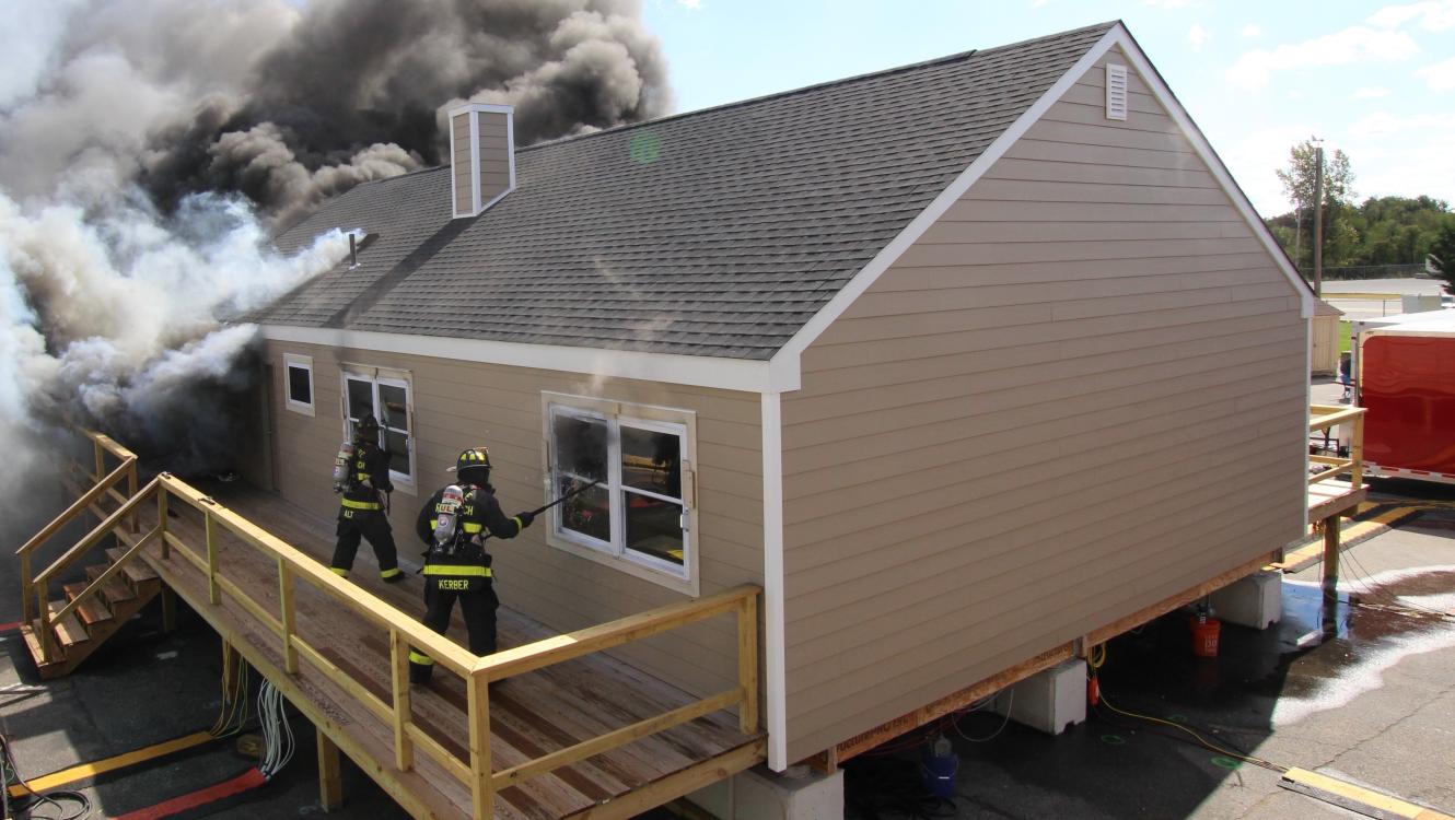house on fire with firefighters opening windows